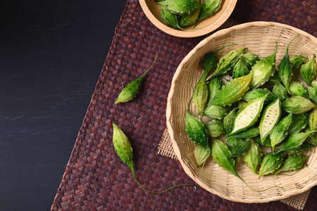 Fresh Organic bitter gourd or bitter melon in a bamboo basket on color woven bamboo sheet, Food ingredients and herbal medicine, Top viewの写真素材