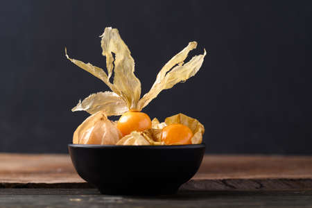 Cape gooseberry or golden berry (Physalis peruviana) in black bowl on wooden background, Healthy tropical fruitの写真素材