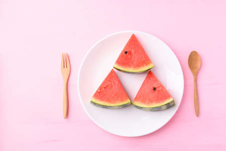 Sliced watermelon on plate with wooden spoon and fork on pink color background, Tropical fruit in summer season, Top viewの写真素材