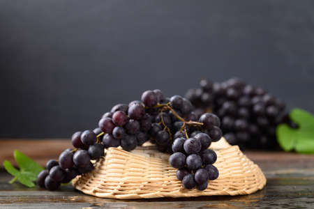 Red grape in bamboo basket on wooden with black backgroundの写真素材