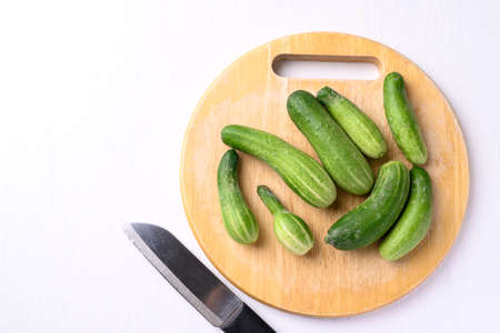 Organic cucumber on cutting wooden board with kitchen knife on white background, Imperfectly shapeの写真素材