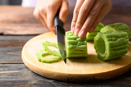 Hand holding knife and cutting bitter melon or bitter gourd for cookingの写真素材