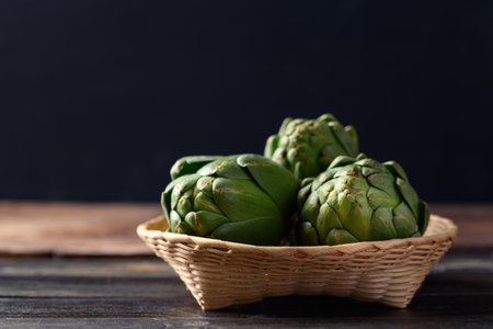 Green artichoke in basket on black background, Edible flower budの写真素材