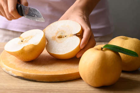 Asian pear or Nashi pear with hand holding knife and cutting on wooden boardの写真素材