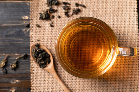 Hot tea in cup glass with dried tea leaves in spoon, Healthy drink, Table top view