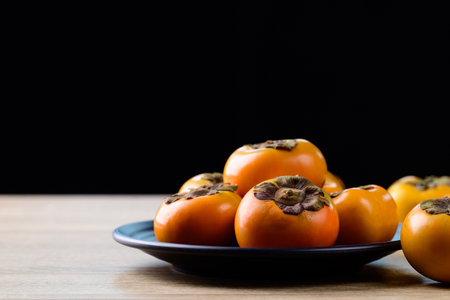 Fresh persimmon fruit on plate with black background, Autumn seasonal fruitの写真素材