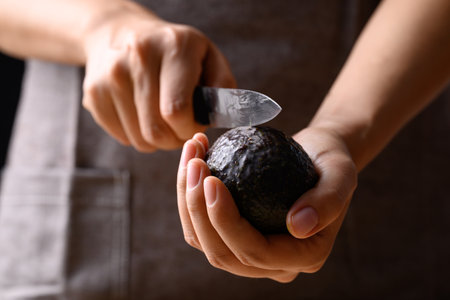 Ripe hass avocado fruit with hand holding knife and cuttingの写真素材