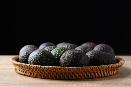 Ripe hass avocado fruit in basket on wooden table with black backgroundの写真素材