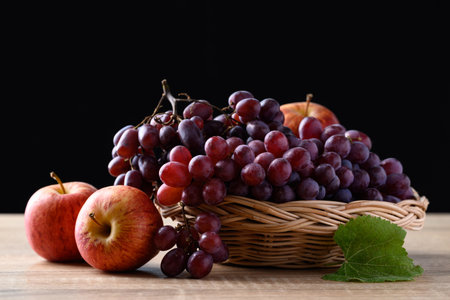 Red grape and apple fruit on wooden table with black background