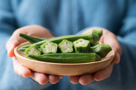 Green okra in wooden bowl holding by hand, Healthy vegetables