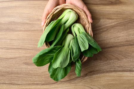 Bok choy or Pak choi (Chinese cabbage) in basket holding by hand on wooden background, Table top viewの写真素材