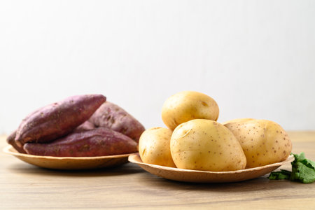 Raw potatoes and purple sweet potatoes on wooden table with white background, Food ingredientの写真素材