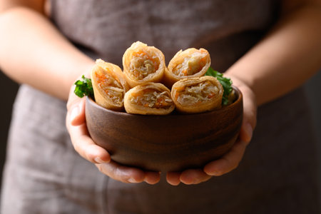 Asian deep fried spring roll filling with cabbage, carrot and glass noodles in wooden bowl holding by handの写真素材
