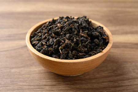 Dried Oolong tea leaves in bowl on wooden background