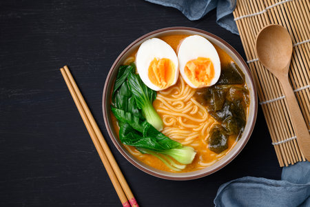 Spicy noodles soup with egg, seaweed and bok choy in bowl on black background, Asian noodles style, Top viewの写真素材