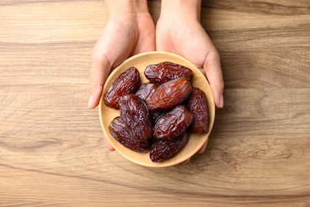 Date palm fruit (MedJool) on wooden plate holding by hand, Table top viewの写真素材