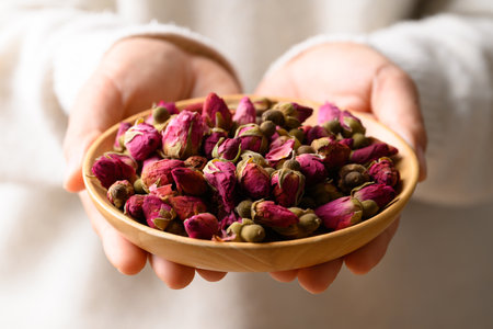 Dried rose bud tea in wooden bowl holding by woman hand, Healthy herbal teaの写真素材