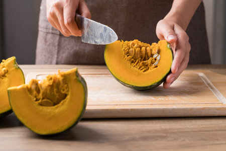 Hand holding kitchen knife and cutting green pumpkin on wooden board.の写真素材