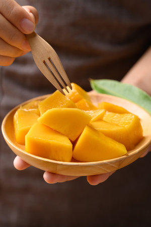 Cube mango on wooden plate holding by hand ready to eating, Tropical fruit in summer seasonの写真素材