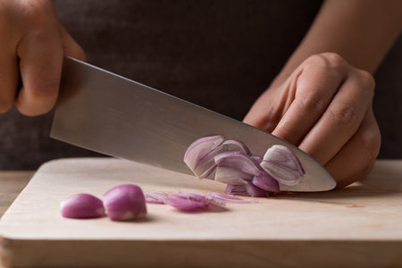Hand holding kitchen knife and slice shallot on wooden board, Homemade cookingの写真素材