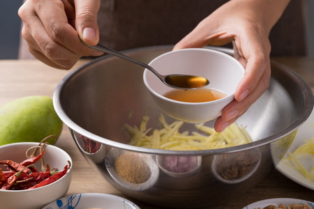 Spicy mango salad cooking, Hand adding fish sauce in bowl and mixing with ingredientsの写真素材