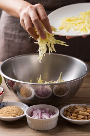 Spicy mango salad cooking, Hand pouring shredded green mango in bowl and mixing with ingredientsの写真素材