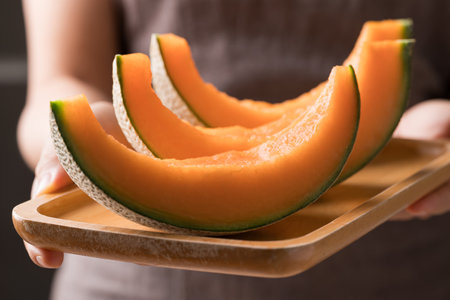 Sliced Orange melon, Musk melon or Flesh melon on plate holding by hand, Fruit in summer seasonの写真素材