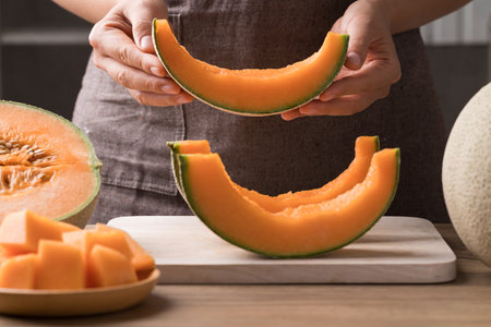 Sliced Orange melon, Musk melon or Flesh melon on cutting wooden board and holding by hand, Fruit in summer seasonの写真素材