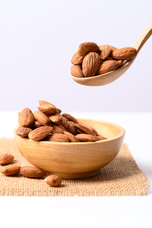 Raw almond nut seed in wooden bowl and spoon on white backgroundの写真素材