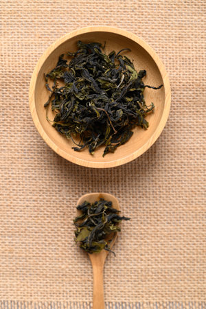 Dried green tea leaves on wooden bowl and spoon, Table top view