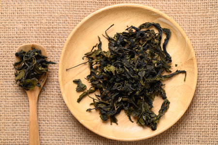 Dried green tea leaves on wooden plate and spoon, Table top view