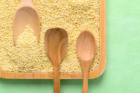 Yellow millet grain in wooden plate with spoon on green background, Food ingredient, Top viewの写真素材