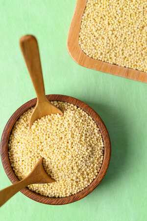 Yellow millet grain in wooden bowl with spoon on green background, Food ingredientの写真素材