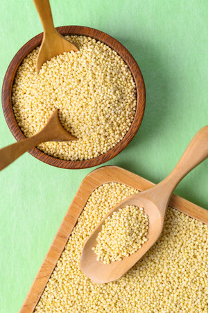 Yellow millet grain in wooden bowl with spoon on green background, Food ingredientの写真素材
