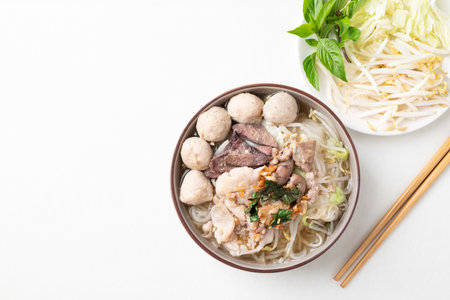 Thai noodles soup with sliced pork, minced pork, meatball and liver in a bowl eating with fresh vegetables on white background, Traditional Thai street food, Top viewの写真素材