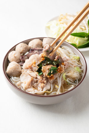 Thai noodles soup with sliced pork, minced pork, meatball and liver in a bowl eating with fresh vegetables on white background, Traditional Thai street foodの写真素材