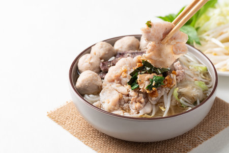 Thai noodles soup with sliced pork, minced pork, meatball and liver in a bowl eating with fresh vegetables on white background, Traditional Thai street foodの写真素材