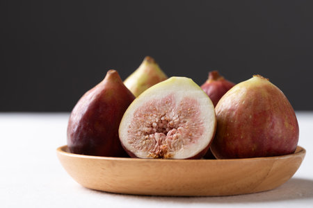 Fresh half fig and whole fruit on wooden plate with white and black background, Autumn fruit