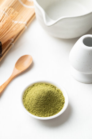 Matcha green tea powder with wooden spoon, bamboo whisk and Chawan bowl on white background