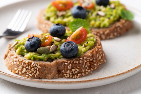 Avocado toast with blueberries, cherry tomatoes, sunflower seeds, pumpkin seeds, sesame seeds and other grain on plate, Healthy eatingの写真素材