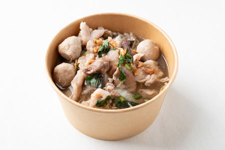 Thai noodles soup with sliced pork, minced pork, meatball in a craft paper bowl on white background,...
