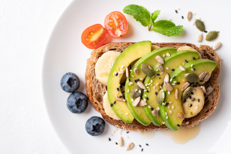 Avocado toast with banana, sunflower seeds, pumpkin seeds, sesame seeds, blueberries, tomatoes and honey on white plate, Healthy eating, Top viewの写真素材