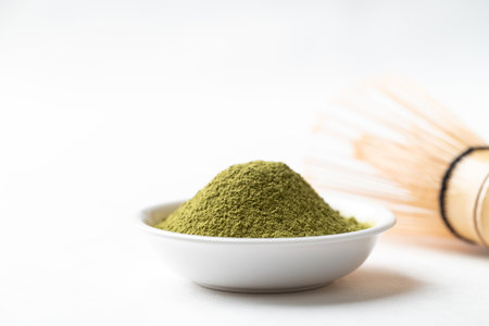 Matcha green tea powder in bowl and bamboo whisk on white background