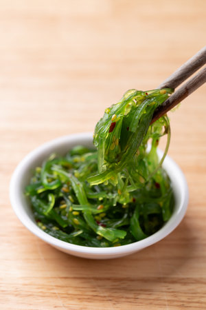 Wakame seaweed salad with sesame seed in a bowl with chopsticks on wooden backgroundの写真素材