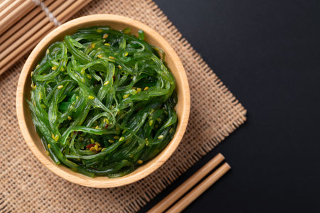 Wakame seaweed salad with sesame seed in a wooden bowl on black background, Top viewの写真素材