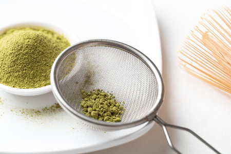 Matcha green tea powder in sieve and bowl on white background