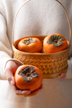 Ripe persimmon fruit in basket holding by hand, Autumn fruitの写真素材