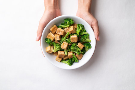 Stir fried tofu and broccoli with soy sauce in bowl holding by hand, Asian vegan food, Top viewの写真素材