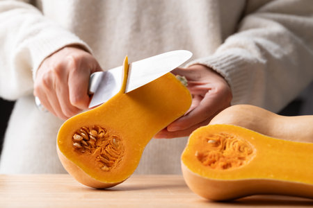 Woman hand holding kitchen knife and peeling butternut squash, Homemade cooking
