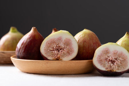 Fresh half fig and whole fruit on wooden plate with white and black background, Autumn fruitの写真素材